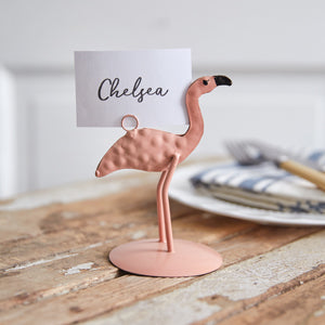 Four metal flamingo card holders with a pink finish, each with a clip to hold cards, adding a whimsical touch to any setting.