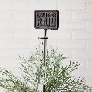 Cast iron rain gauge in a garden setting, featuring a clear plastic tube for measuring rainfall, adding charm and whimsy.