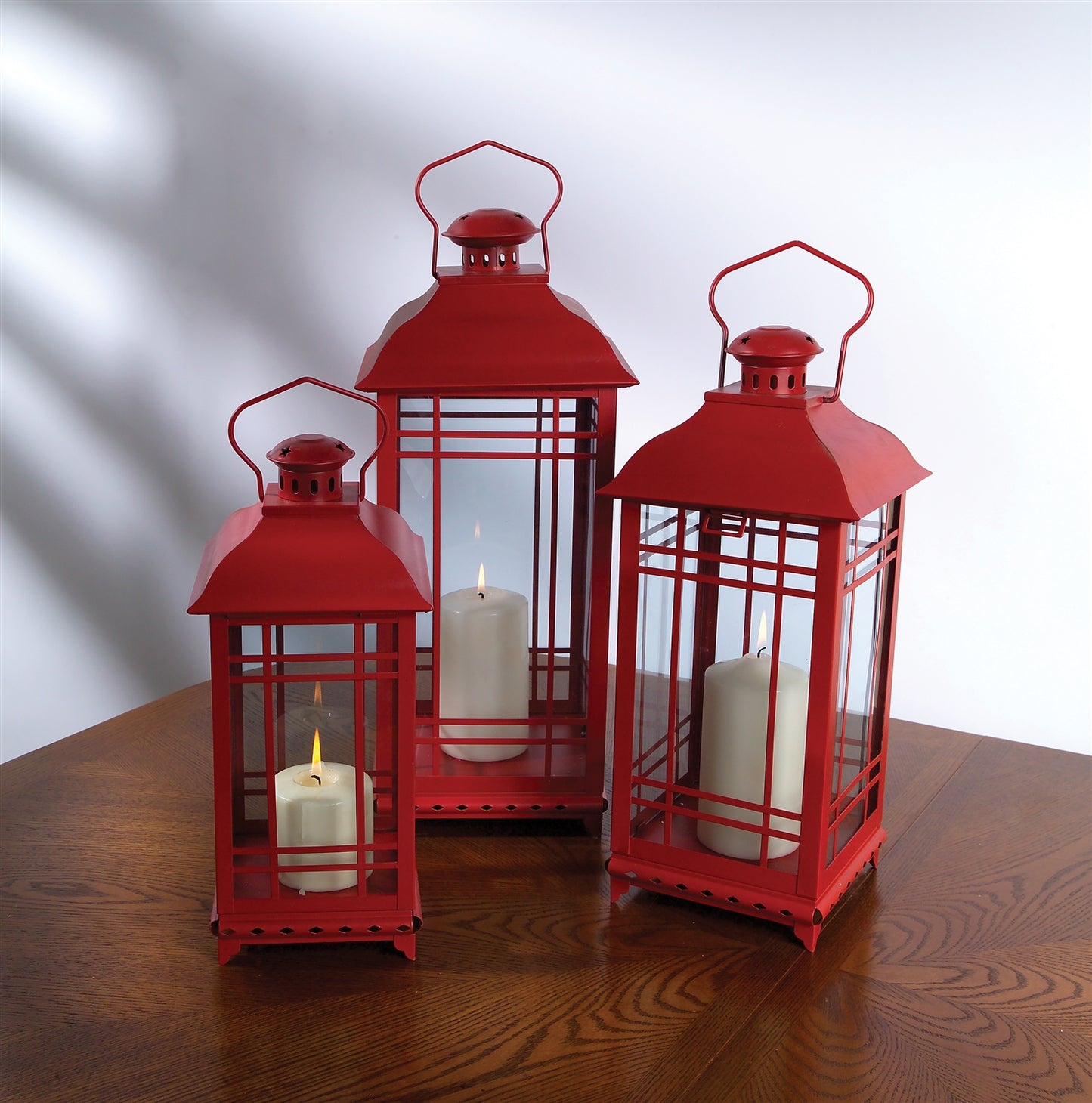 Set of three red metal lanterns with glass panels, classic design, displayed on a wooden surface, ideal for candles or decor.