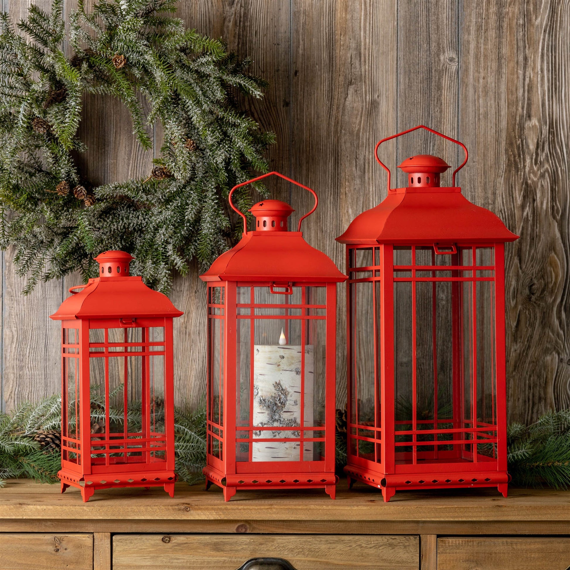 Set of three red metal lanterns with glass panels, classic design, displayed on a wooden surface, ideal for candles or decor.