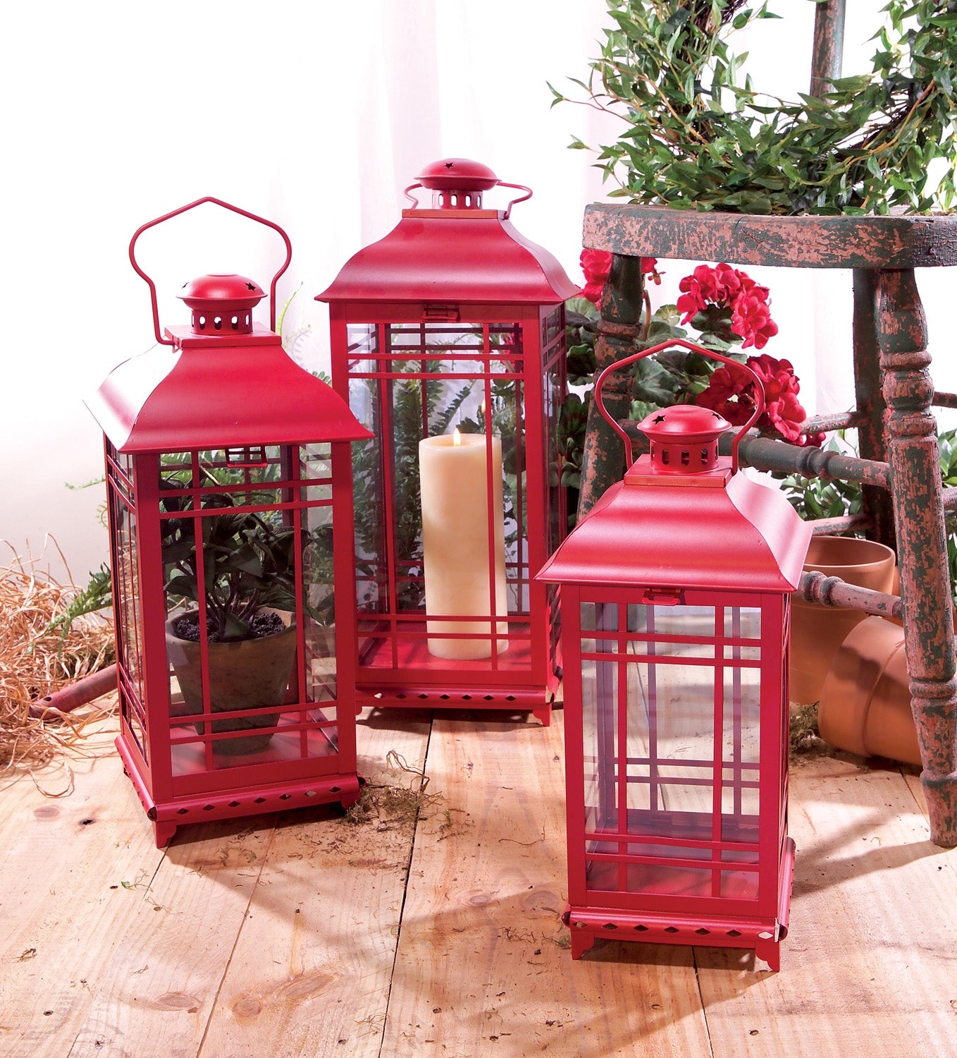 Set of three red metal lanterns with glass panels, classic design, displayed on a wooden surface, ideal for candles or decor.