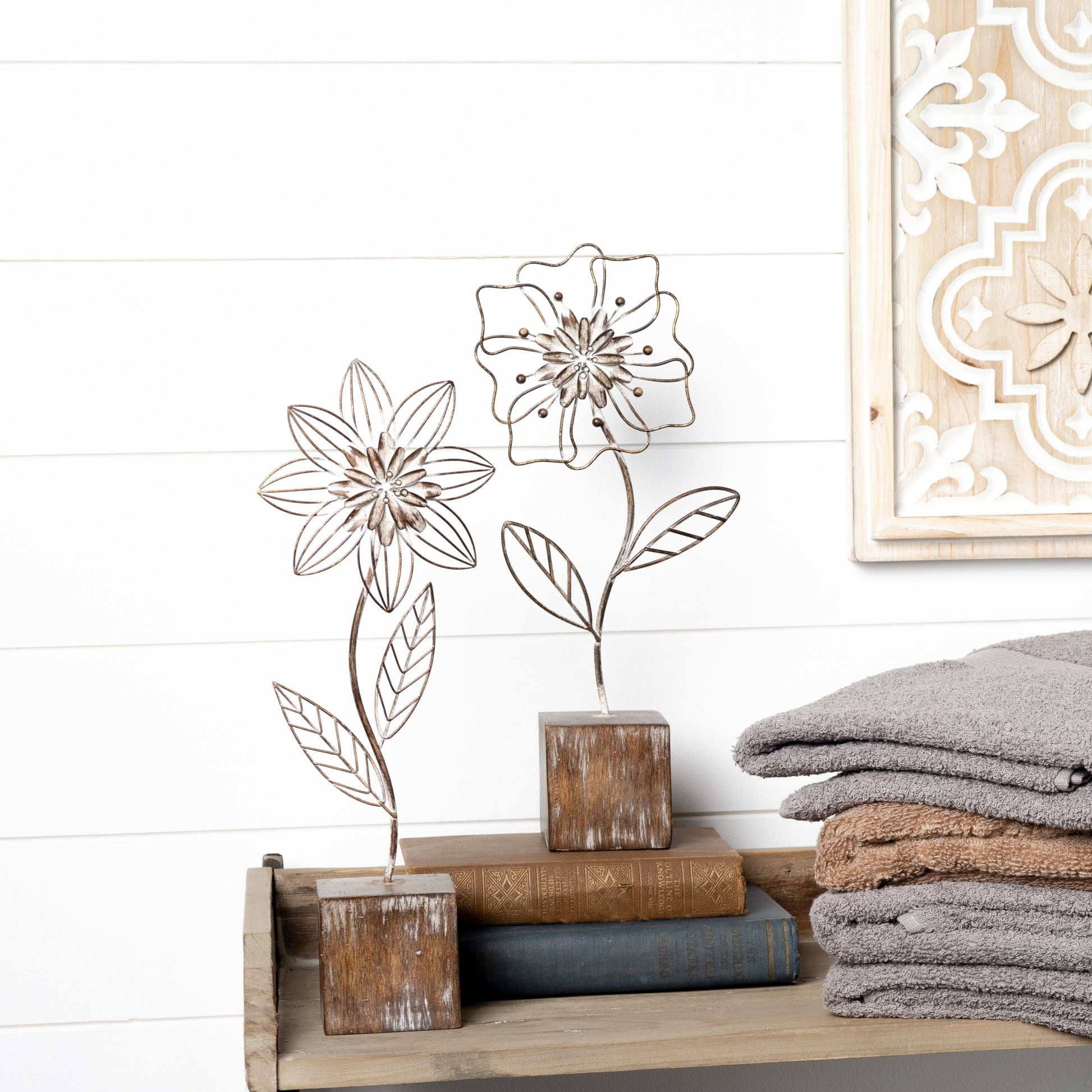 Metal floral decor with intricate flower design on a distressed white-washed base, featuring rustic brown and white tones.