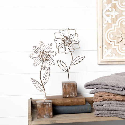 Metal floral decor with intricate flower design on a distressed white-washed base, featuring rustic brown and white tones.