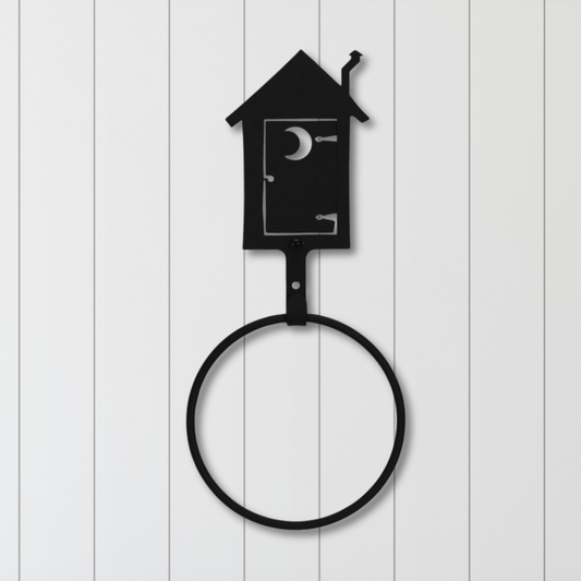 Black metal towel ring shaped like an outhouse on a white wooden background