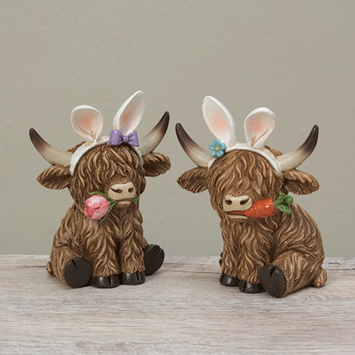 Two resin Highland cows with long brown hair, wearing bunny ear headbands; one holds a carrot, the other a pink rose.