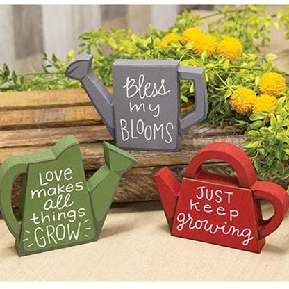 Three colorful wooden watering can sitters with inspiring messages, perfect for adding a whimsical touch to any space.