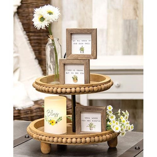 Natural wood two-tiered tray with round bead detailing, black metal center dowel, and three wooden legs for a farmhouse look.