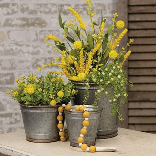 Set of three round galvanized silver metal planters with distressed copper edges, filled with vibrant plants on a porch.