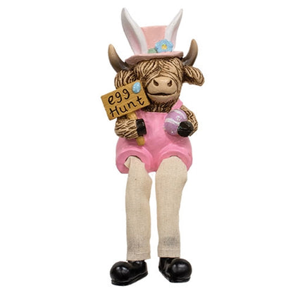Highland cow figurines in pastel overalls and hats, with dangling fabric legs, holding Easter-themed items like eggs and carrots.