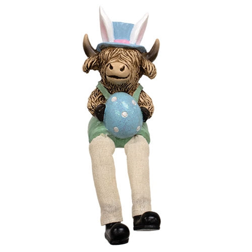 Highland cow figurines in pastel overalls and hats, with dangling fabric legs, holding Easter-themed items like eggs and carrots.