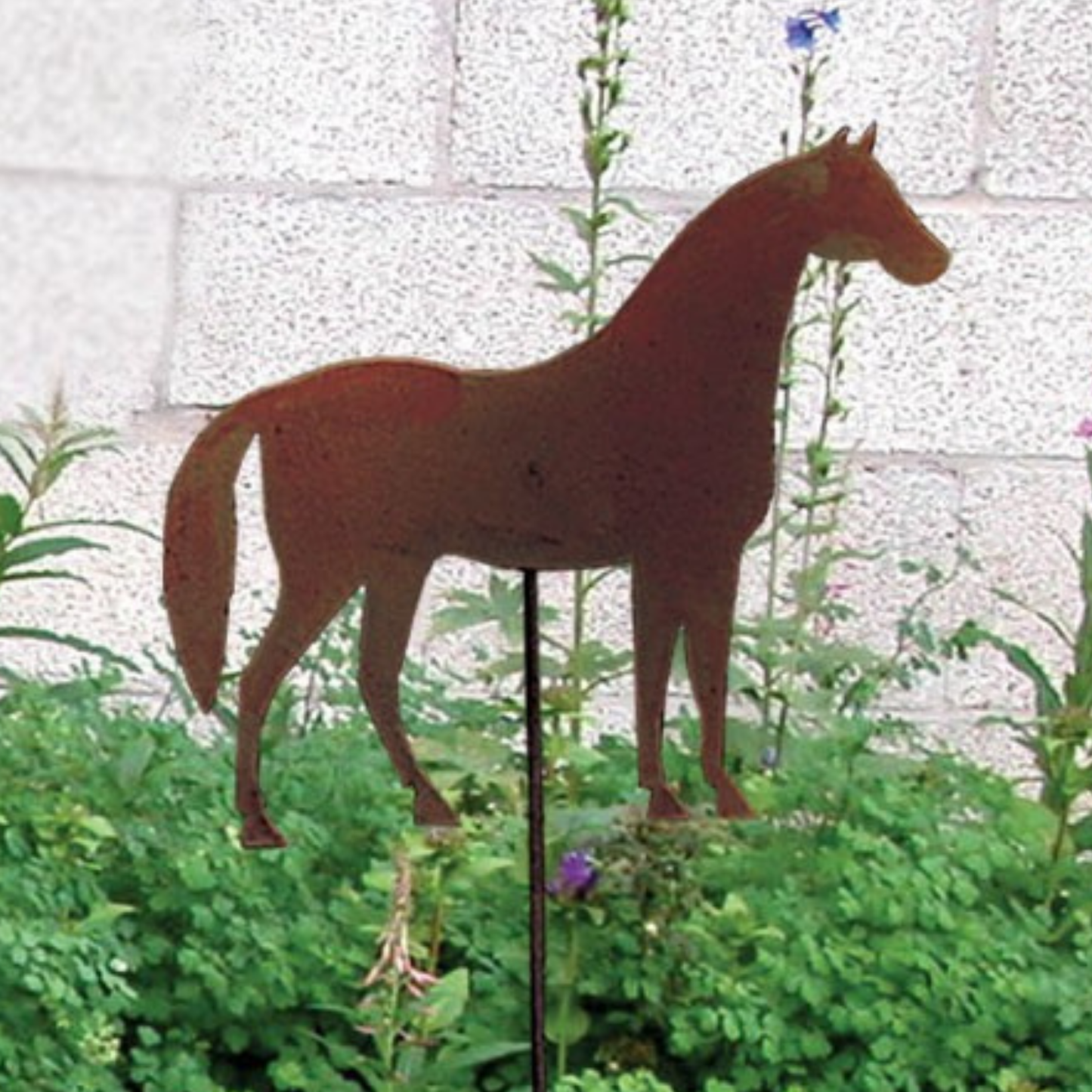 Rust-colored horse-shaped garden stake in a garden setting with a white wall background