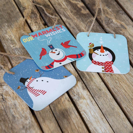 Three charming snowmen tags with festive designs hang against a holiday-themed background, perfect for Christmas decor.